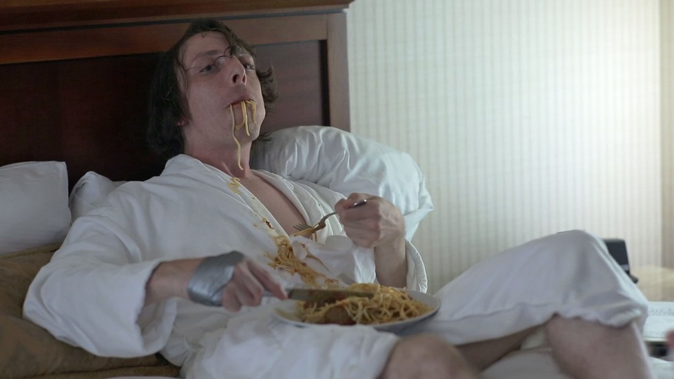 Actor with Taped Hands in bed in a robe, and eating a plate of pasta
